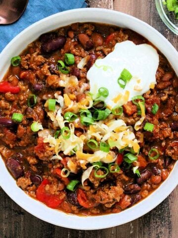 Bowl of hearty pumpkin chili topped with cheese, sour cream and scallions
