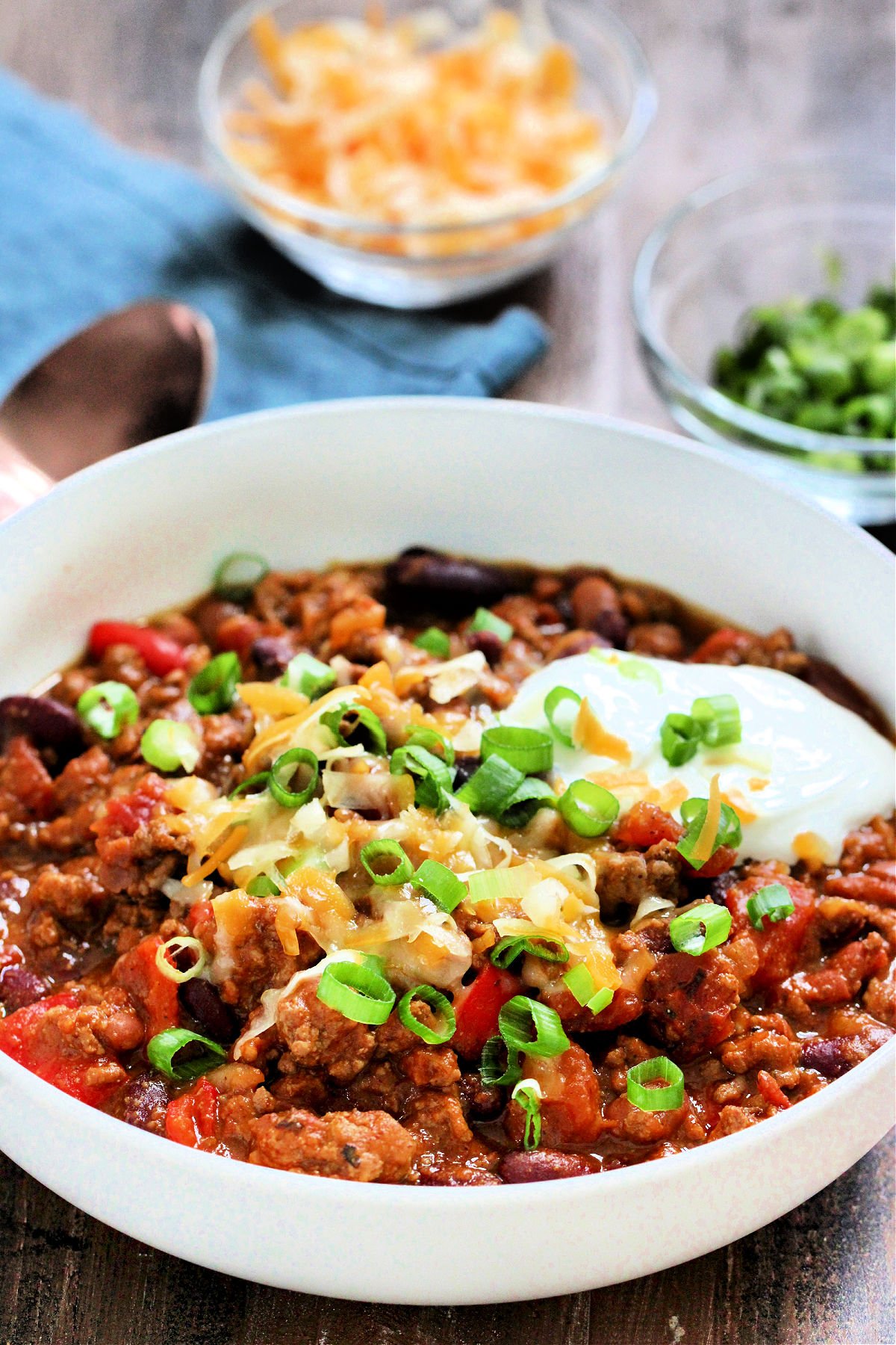 A bowl of hearty pumpkin chili topped with cheese, sour cream, and scallions